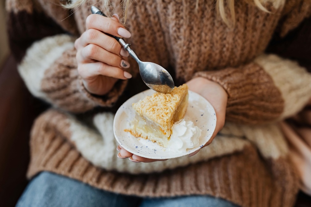 Woman in a pullover eating an apple pie. The woman's face is not visible.